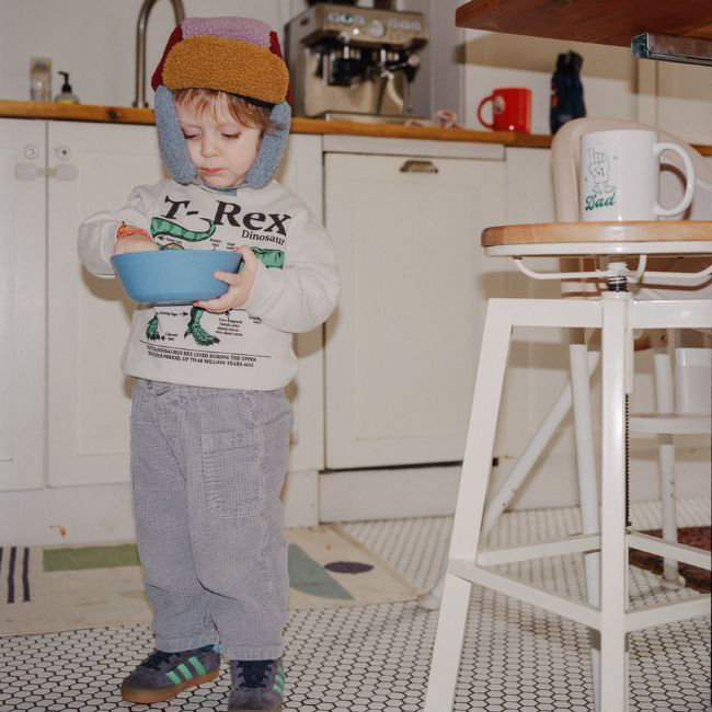 Child wearing winter clothing and holds a mixing bowl in a kitchen